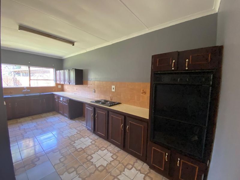 A spacious kitchen featuring dark wood cabinetry, a built-in oven, hob, and tiled finishes, offering a functional layout ready for modernization.