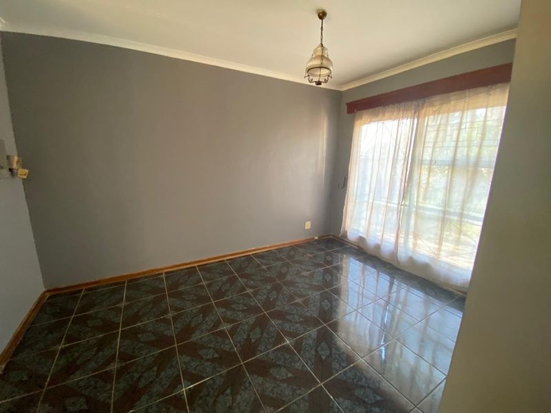 An empty bedroom featuring dark patterned floor tiles, grey walls, and a large window with security bars and a curtain rail.