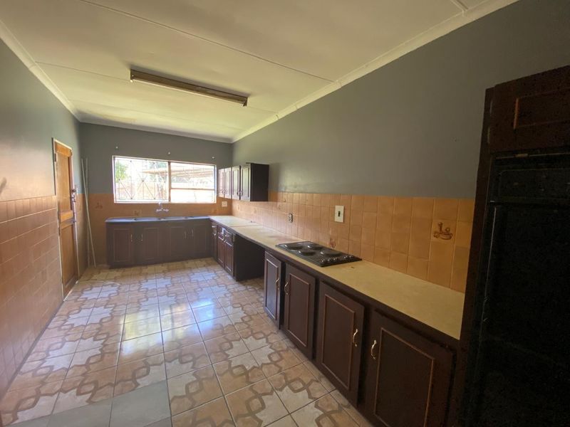 A spacious, empty kitchen featuring dark built-in cabinetry, a tiled splashback, and an integrated electric hob, offering a functional layout ready for modernization.