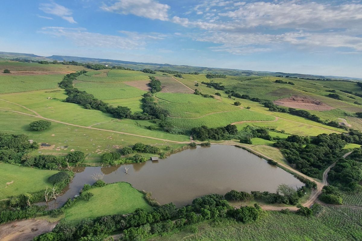 An aerial view of the small holding property featuring a large dam, expansive green pastures, and surrounding agricultural land.