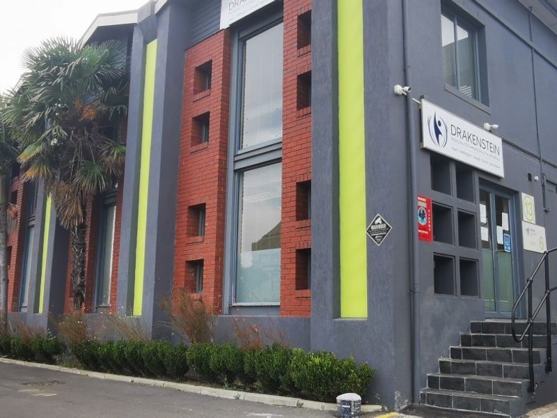 Exterior view of a modern office building featuring a brick and painted facade, large windows, and a paved entrance with concrete stairs.