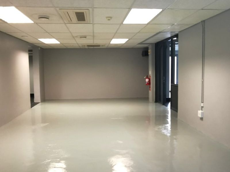 A spacious, empty office area featuring a clean epoxy floor, suspended ceiling with recessed lighting, and integrated air conditioning.