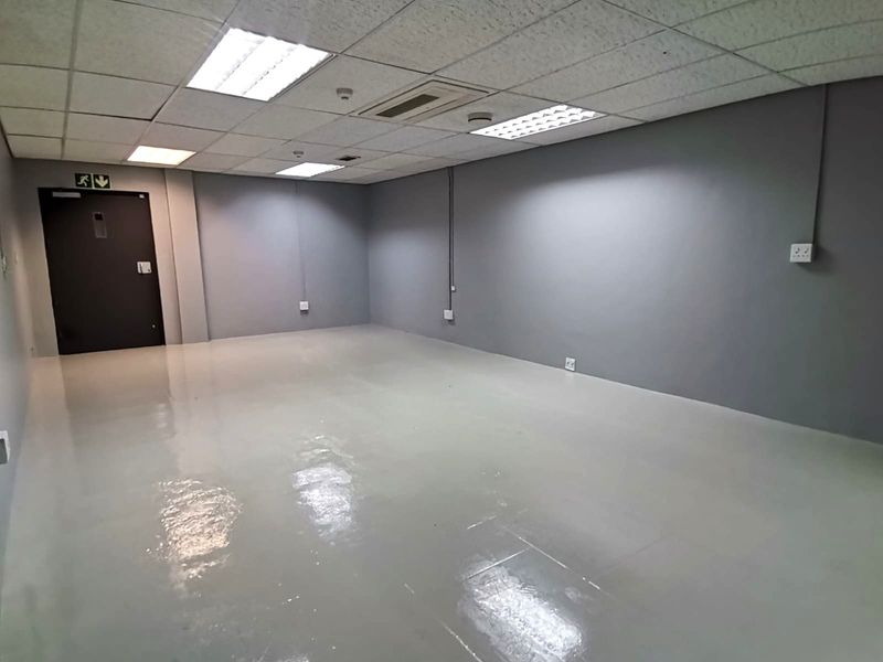 A clean, empty office space featuring a suspended ceiling with recessed lighting, ducted air conditioning, and durable epoxy flooring.