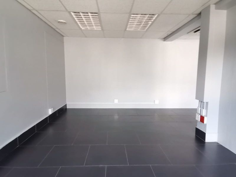 A clean, vacant office space featuring modern dark tiled flooring, a suspended ceiling with recessed lighting, and integrated electrical trunking for connectivity.
