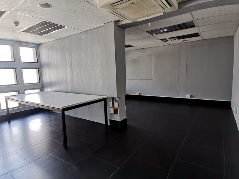 An open-plan office space featuring dark tiled flooring, suspended ceilings with recessed lighting, and a ceiling-mounted air conditioning unit.