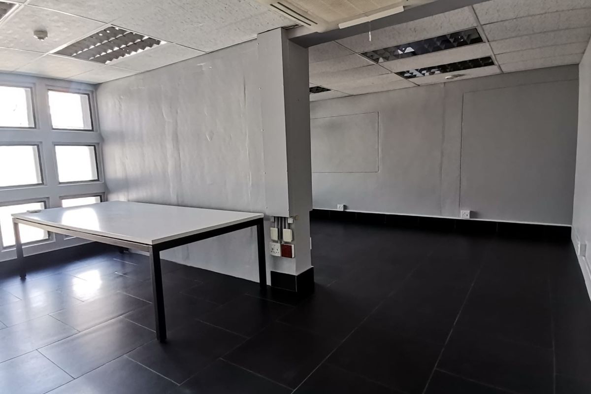 An open-plan office space featuring dark tiled flooring, suspended ceilings with recessed lighting, and a ceiling-mounted air conditioning unit.