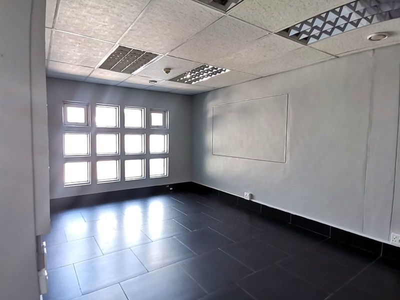 A vacant office space featuring dark tiled flooring, a suspended ceiling with recessed lighting, and a grid window configuration providing natural light.