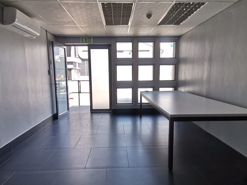 A functional, empty office space featuring tiled flooring, a split-system air conditioner, recessed ceiling lighting, and large windows providing natural light.
