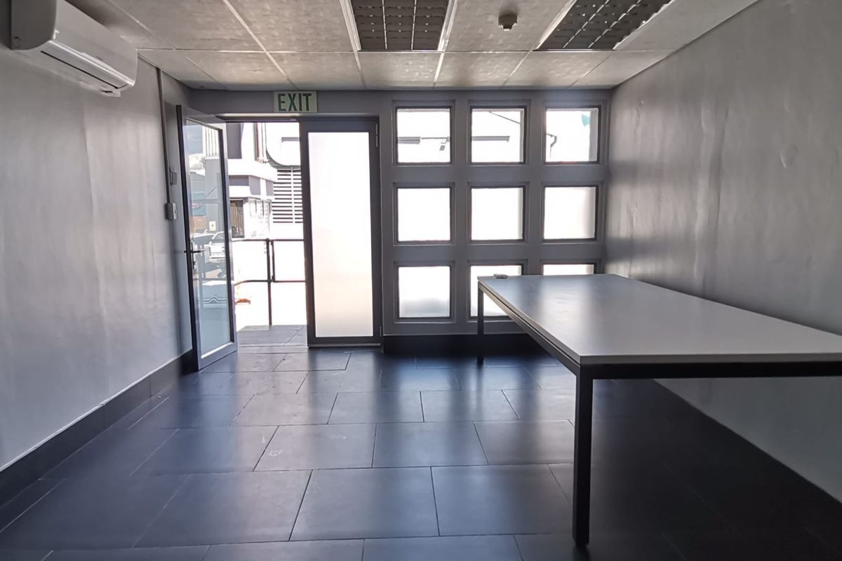 A functional, empty office space featuring tiled flooring, a split-system air conditioner, recessed ceiling lighting, and large windows providing natural light.