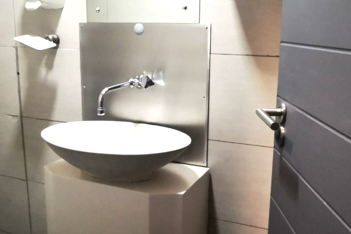 A compact office bathroom featuring a modern vessel sink, wall-mounted faucet, stainless steel splashback, and tiled wall finishes.