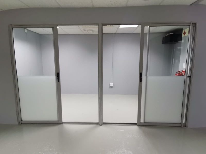 A clean, empty office space featuring modern aluminium sliding glass doors with frosted privacy panels and a functional suspended ceiling.