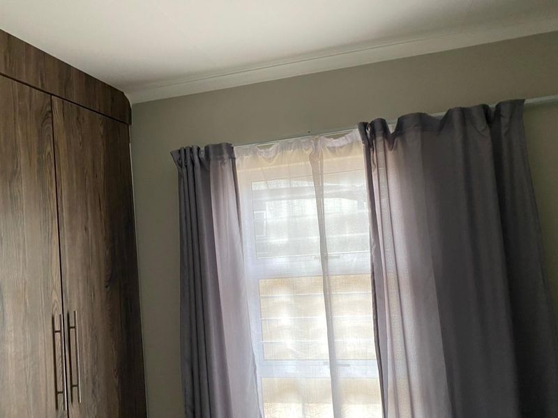A bedroom interior featuring dark wood-finish built-in cupboards and a window fitted with horizontal blinds and curtains.