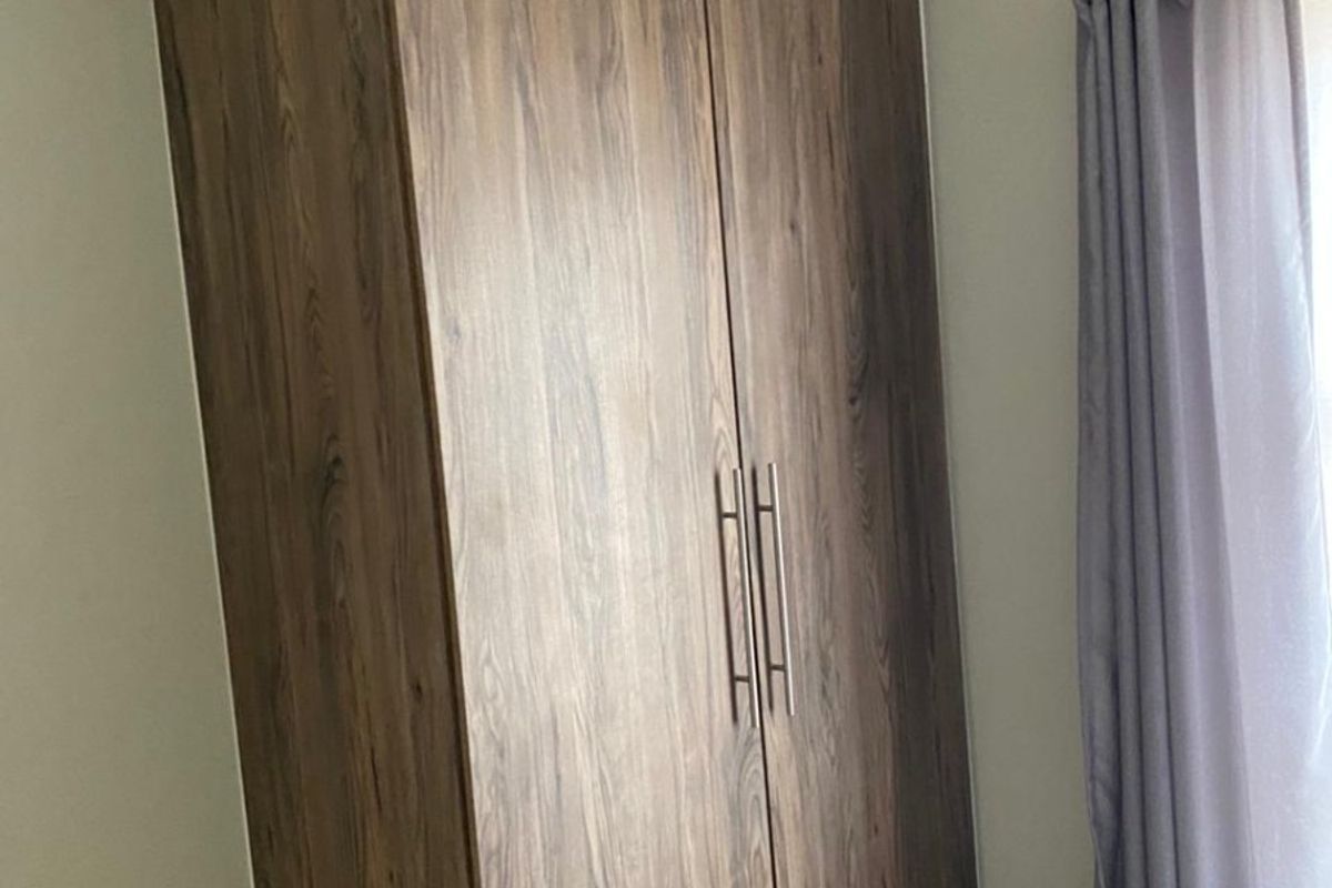 A bedroom featuring a modern wood-grain built-in wardrobe with sleek metal handles and neutral tiled flooring.