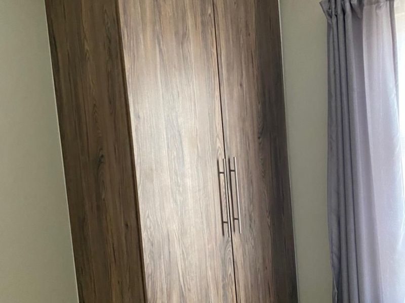A bedroom featuring a modern wood-grain built-in wardrobe with sleek metal handles and neutral tiled flooring.