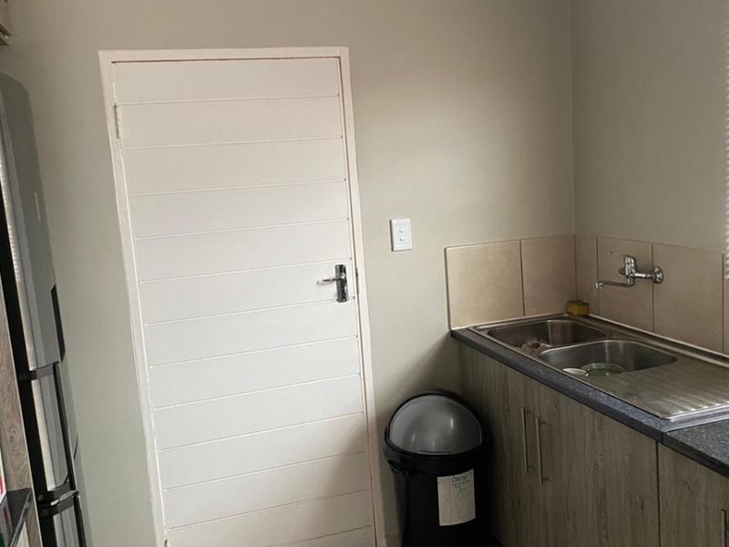 A functional scullery area featuring a stainless steel sink, tiled splashback, and modern laminate cabinetry with tiled flooring.