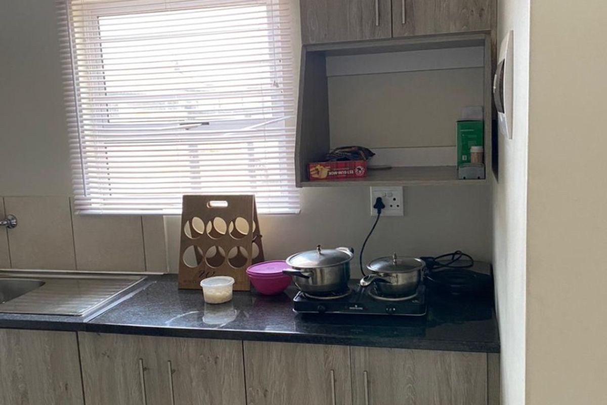 A compact kitchen featuring modern wood-look laminate cabinetry, dark granite countertops, a stainless steel sink, and neutral tiled flooring.