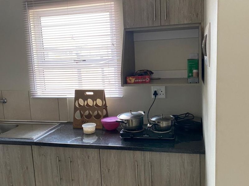 A compact kitchen featuring modern wood-look laminate cabinetry, dark granite countertops, a stainless steel sink, and neutral tiled flooring.