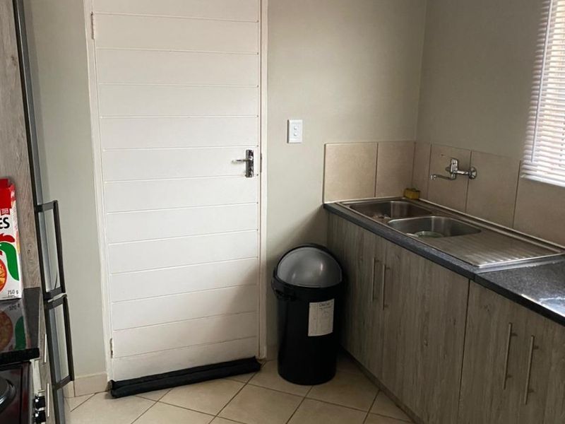 A functional scullery area featuring laminate cabinetry, granite countertops, a double stainless steel sink, and tiled flooring.