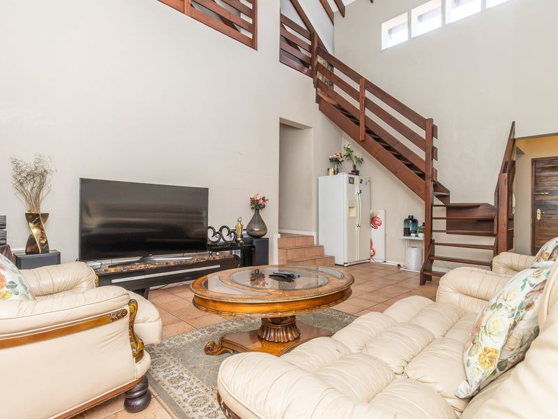 Spacious living room featuring high vaulted ceilings, tiled flooring, and a prominent wooden staircase leading to a mezzanine level.