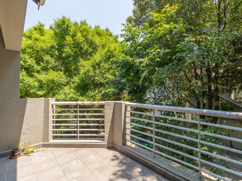 A private balcony featuring tiled flooring and a metal balustrade, offering a peaceful outlook over mature trees.