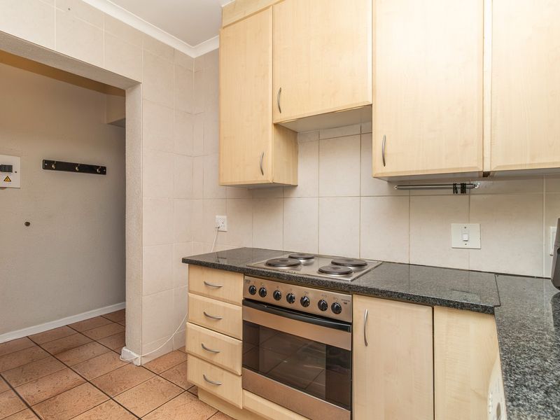 Functional kitchen featuring light wood cabinetry, granite countertops, built-in oven and hob, and tiled splashbacks, leading into an adjacent hallway area.