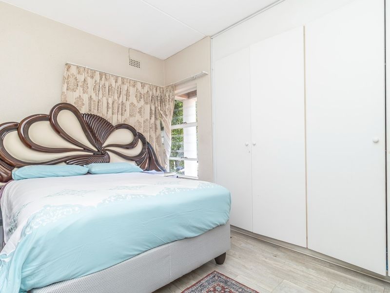 A bedroom featuring built-in cupboards, laminate flooring, and a window with curtains.