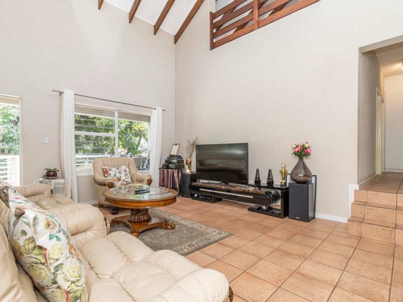 Spacious living room featuring high vaulted ceilings with exposed timber rafters, tiled flooring, and a mezzanine loft level overlooking the main area.