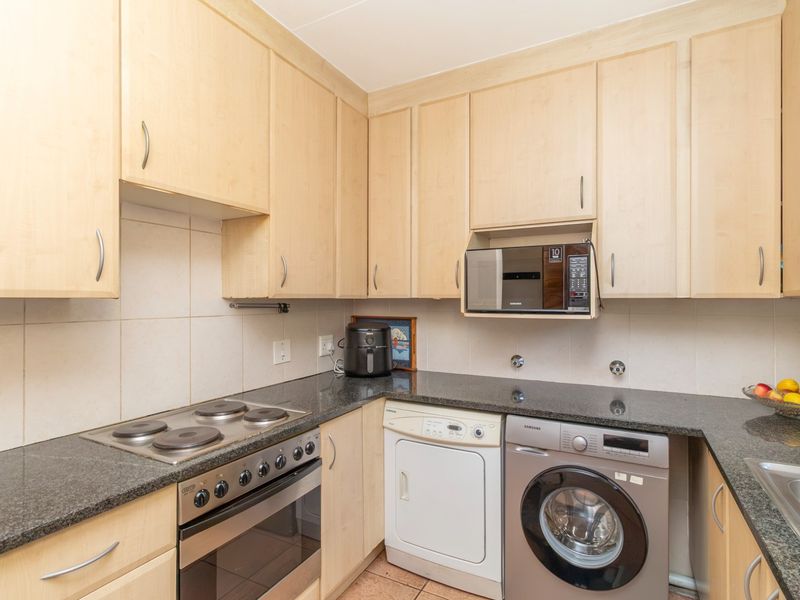 A functional kitchen featuring light wood cabinetry, granite countertops, a built-in electric oven and hob, and tiled backsplash with integrated appliance spaces.