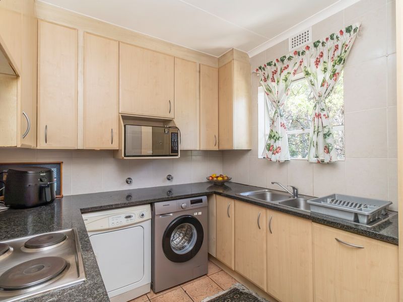 Functional kitchen featuring light wood cabinetry, granite countertops, a double basin sink, and integrated electric hob with space for laundry appliances.