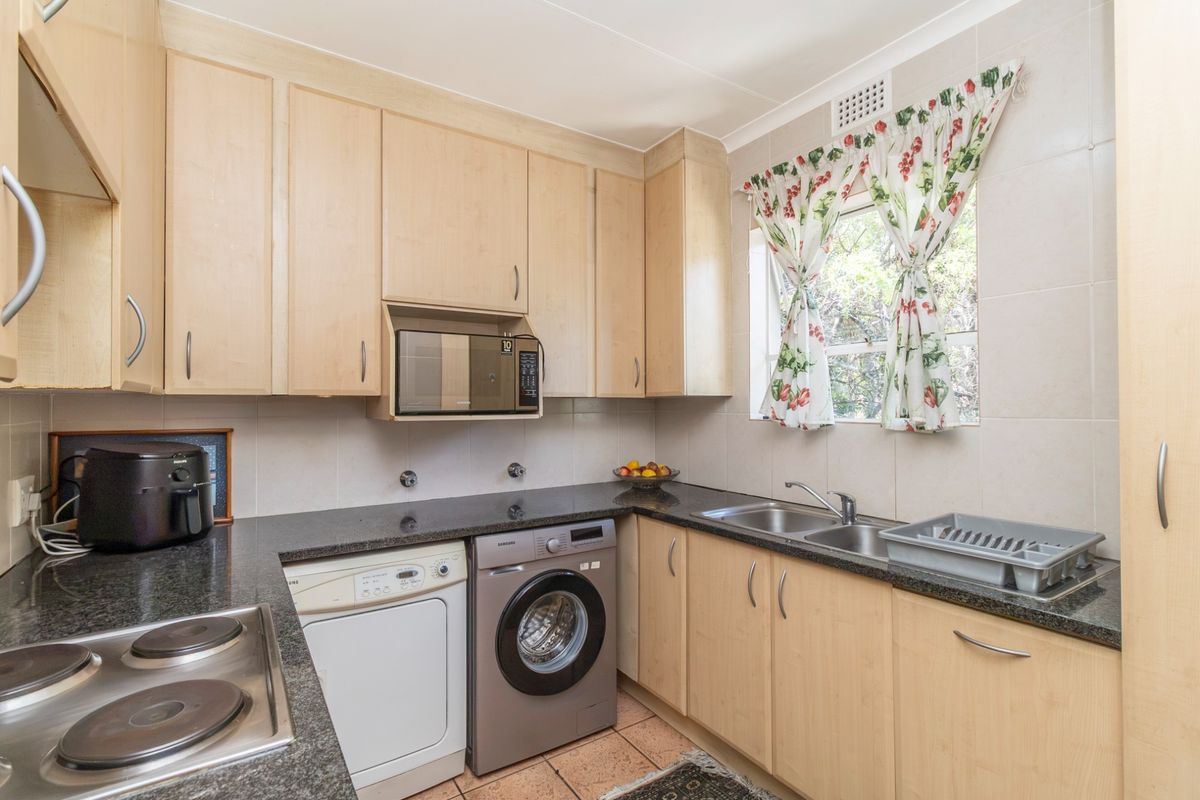 Functional kitchen featuring light wood cabinetry, granite countertops, a double basin sink, and integrated electric hob with space for laundry appliances.
