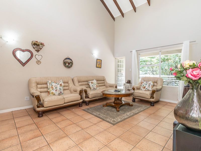 Spacious living room featuring high vaulted ceilings with exposed timber beams, tiled flooring, and large windows providing natural light and access to the outdoors.