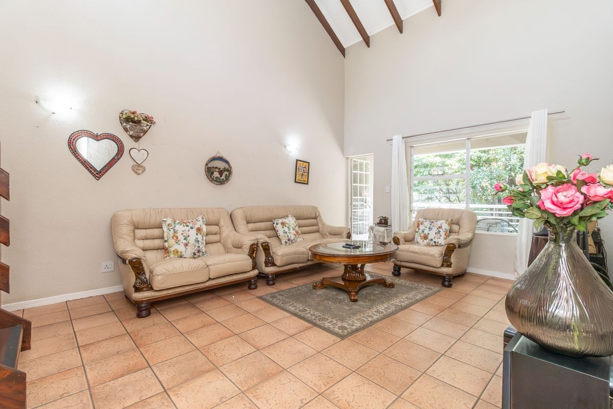 Spacious living room featuring high vaulted ceilings with exposed timber beams, tiled flooring, and large windows providing natural light and access to the outdoors.