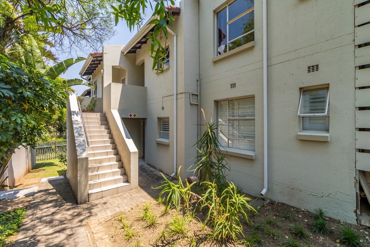 Rear exterior view of the apartment building featuring an external staircase, paved walkway, and established garden area.