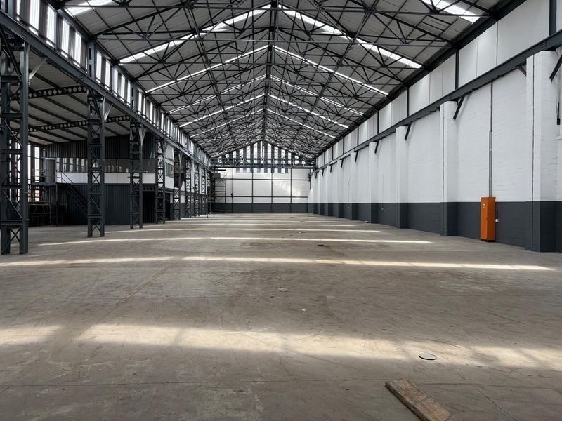 Expansive industrial warehouse space featuring high ceilings with exposed steel trusses, concrete flooring, and abundant natural light through integrated skylights.