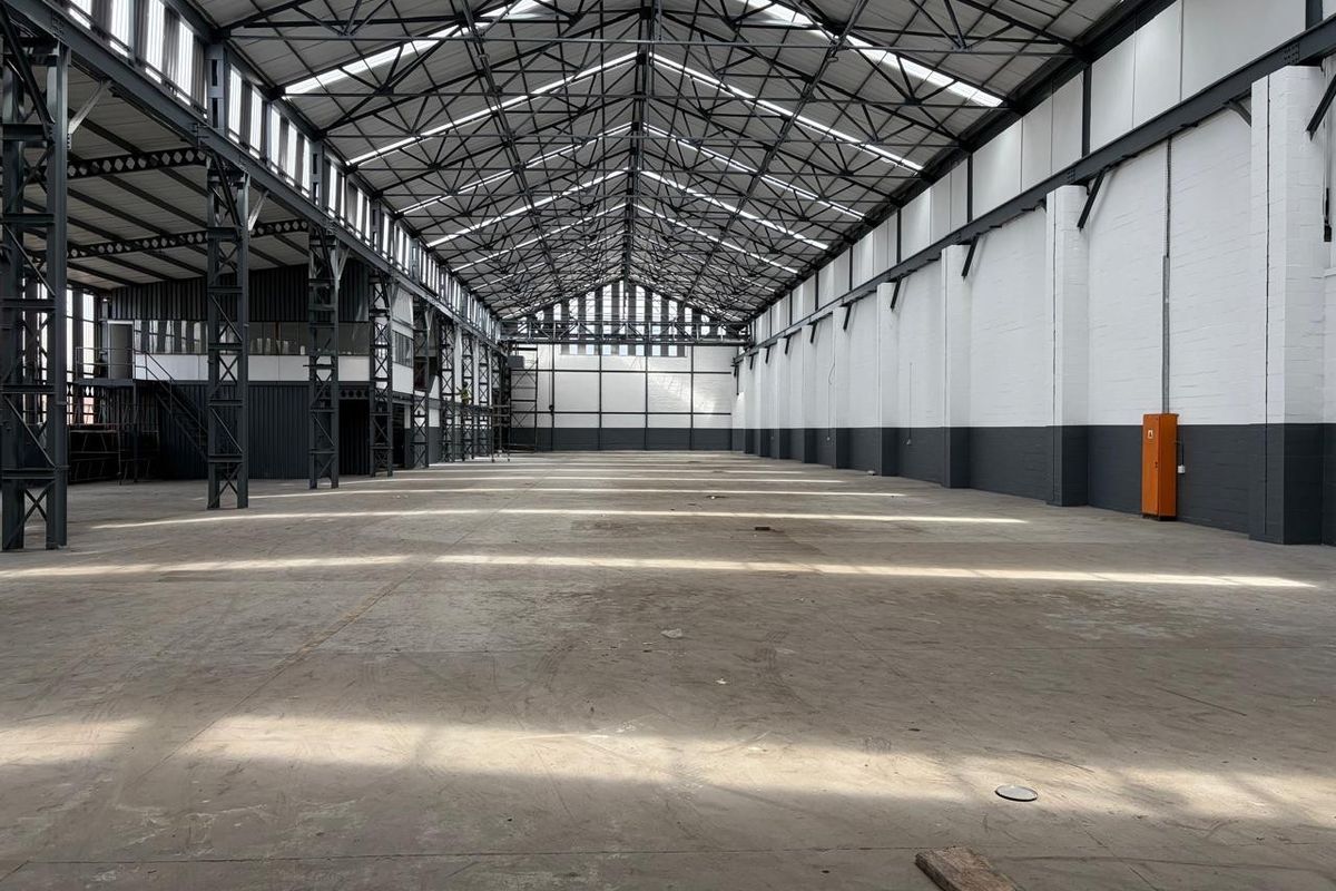Expansive industrial warehouse space featuring high ceilings with exposed steel trusses, concrete flooring, and abundant natural light through integrated skylights.
