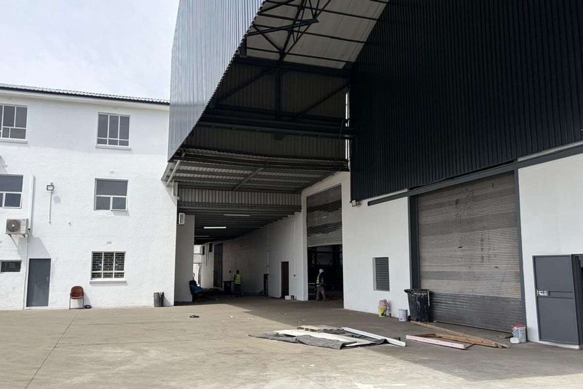 Industrial property exterior featuring a large concrete yard, high-clearance steel roof structure, and multiple roller shutter doors for efficient loading and access.
