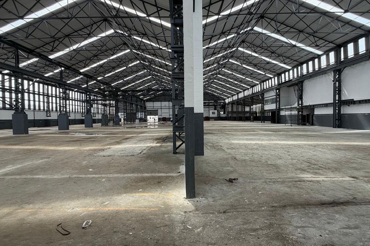 Spacious industrial warehouse featuring high exposed steel truss ceilings, abundant natural light from skylights, and durable concrete flooring throughout the open-plan facility.