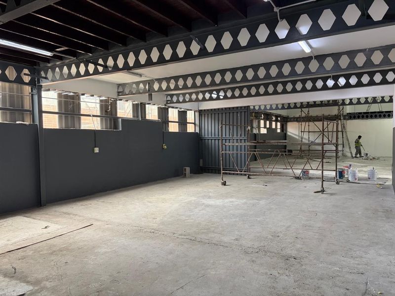 Spacious industrial utility area featuring exposed steel lattice beams, concrete flooring, and high ceilings, currently undergoing renovation.
