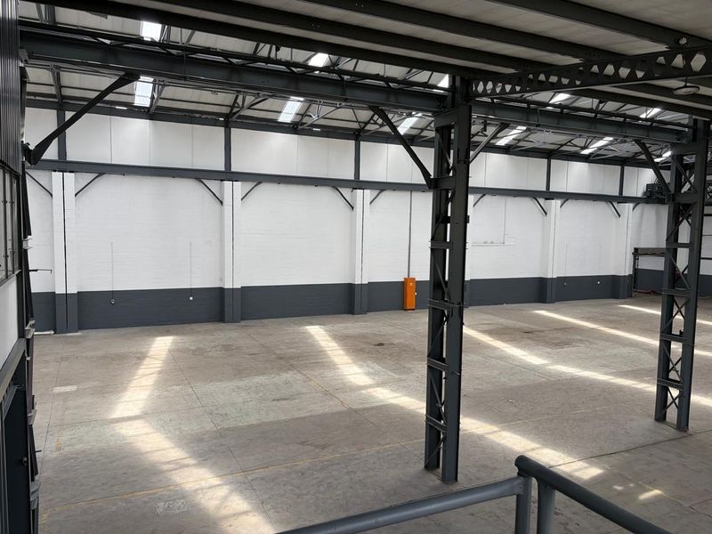 Spacious industrial warehouse unit featuring high ceilings with exposed steel trusses, abundant natural light from skylights, and durable concrete flooring.