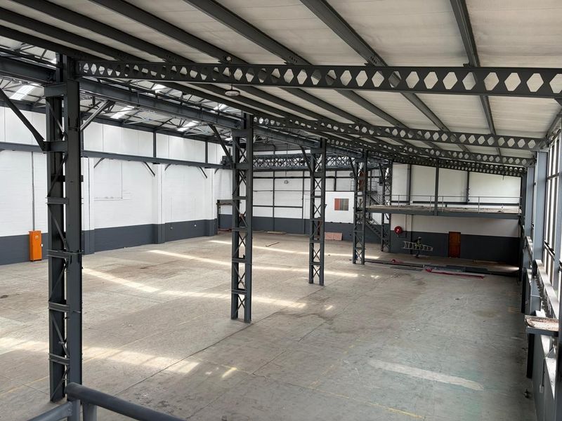 Spacious industrial warehouse featuring a high-clearance steel portal frame, concrete flooring, integrated mezzanine level, and ample natural light through overhead skylights.