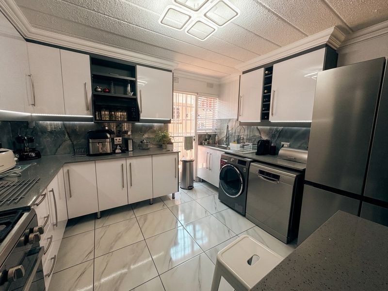 Modern kitchen featuring high-gloss white cabinetry, stone countertops, marble-look tiled flooring, and integrated lighting, providing a clean and functional culinary space.