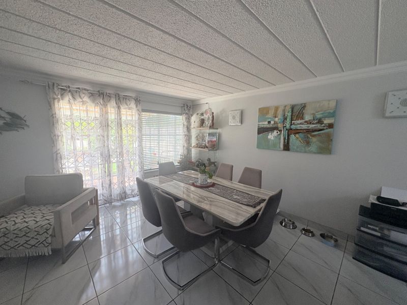 A bright dining room featuring large format floor tiles, a textured ceiling, and a sliding glass door providing access to the outdoor area.