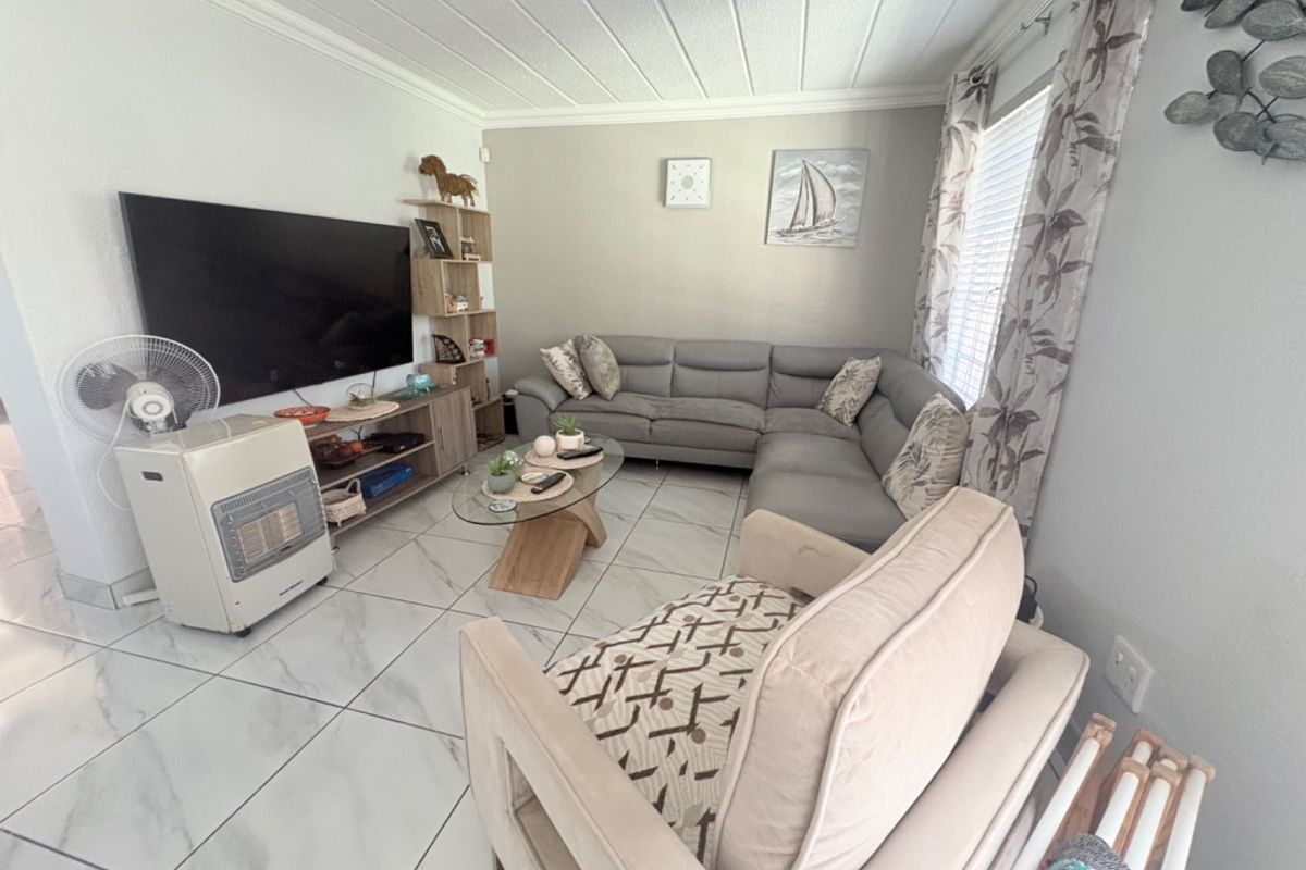 A comfortable living room featuring light-colored marble-look floor tiles, coved ceilings, and neutral wall tones, creating a bright and inviting space.