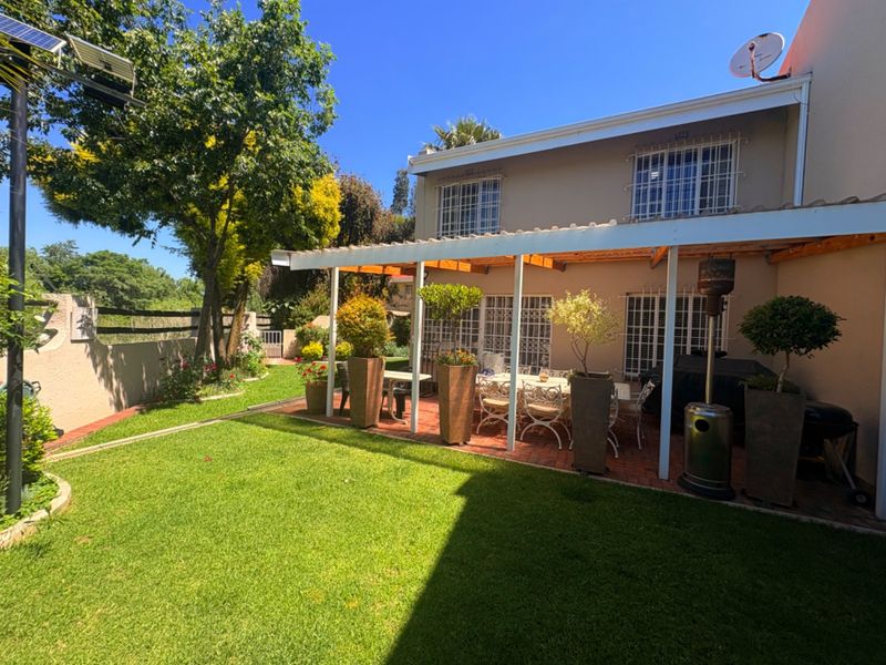 A well-maintained rear garden featuring a paved covered patio area, established lawn, and secure window treatments.