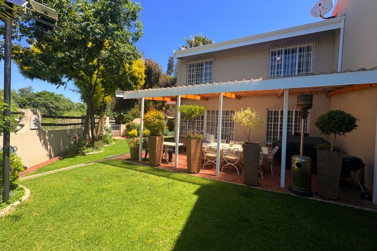 A well-maintained rear garden featuring a paved covered patio area, established lawn, and secure window treatments.
