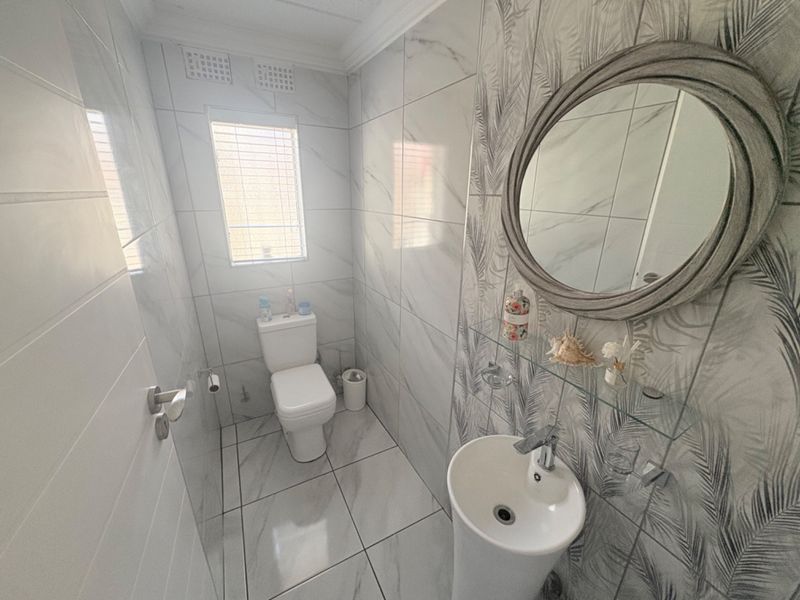 A modern, compact bathroom featuring marble-look wall and floor tiles, a pedestal basin, and a wall-mounted toilet.