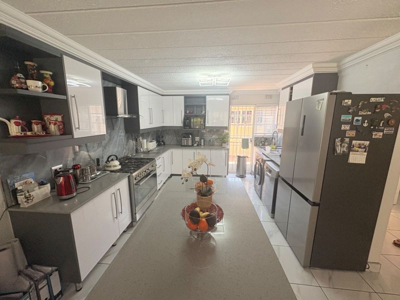 Modern kitchen featuring a central island with quartz countertops, sleek white and grey cabinetry, gas stove, and tiled flooring with direct access to the rear.