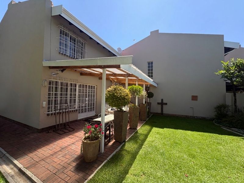 Rear exterior view featuring a covered patio with brick paving, a small lawn area, and security bars on the windows.