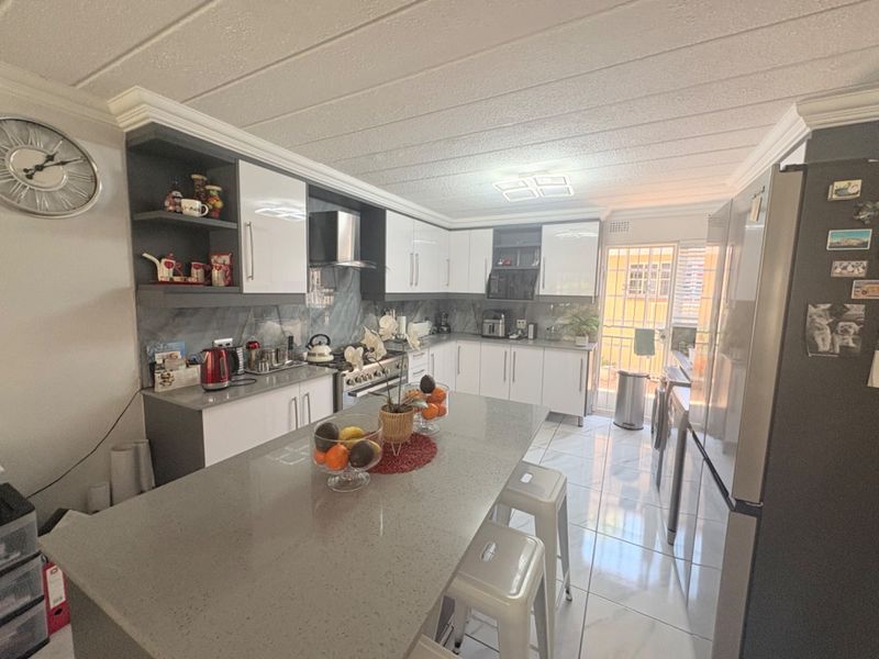 Modern kitchen featuring white cabinetry, grey quartz countertops, a central island, and tiled flooring with direct access to an outdoor area.