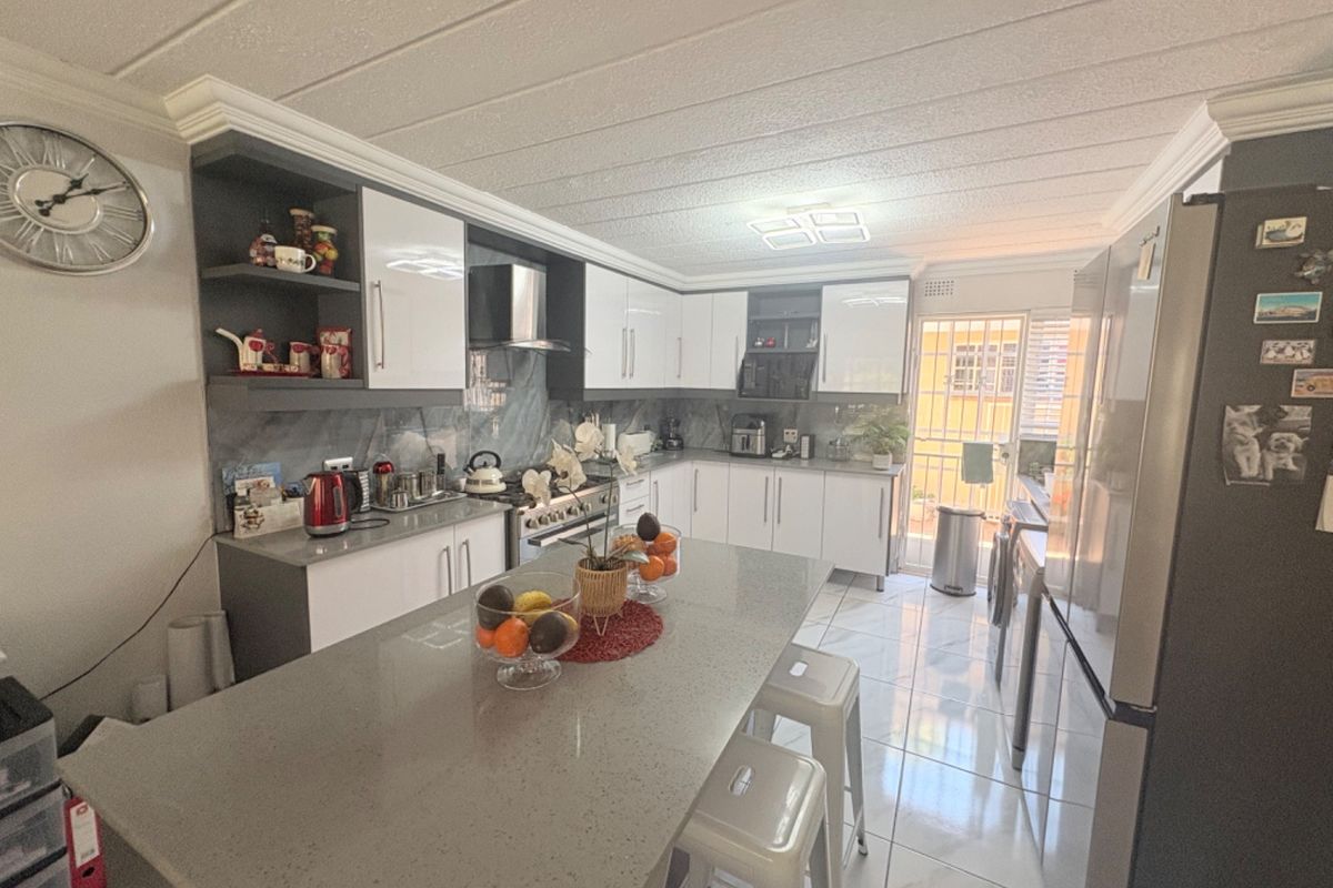 Modern kitchen featuring white cabinetry, grey quartz countertops, a central island, and tiled flooring with direct access to an outdoor area.